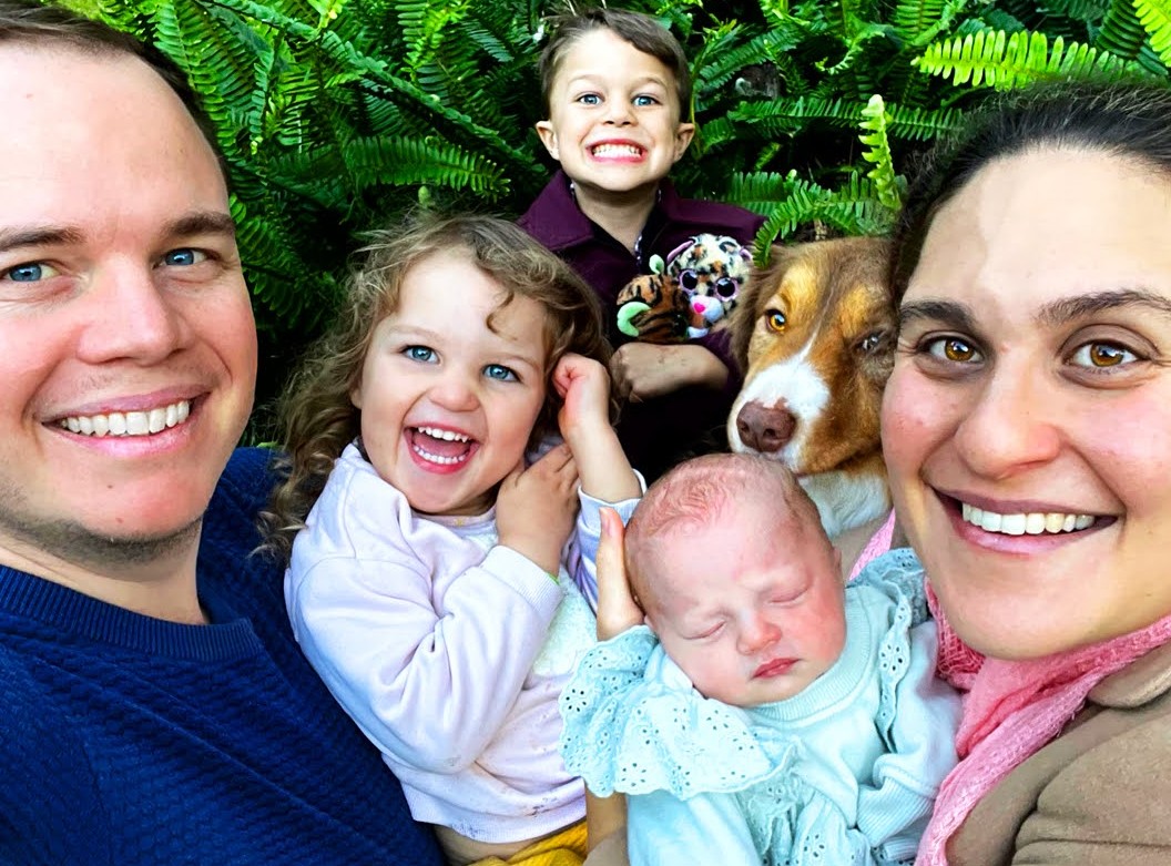 Telissia with her husband, three children and their border collie Paxi, laughing together outdoors